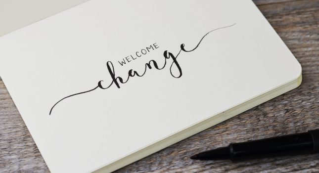 WELCOME CHANGE hand lettering in notebook with pen on wooden bac